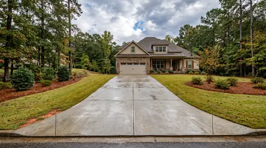 Broom-finished concrete driveway running up to a two-car garage at a stacked-stone and stucco home in Savannah, GA, after a rain shower.