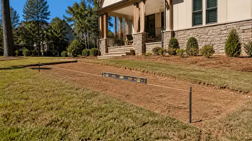 Backyard grade checked with a level and string before a patio pour at a stacked-stone and stucco home in Savannah, GA, in clear late-morning sun.