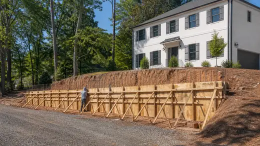 Retaining wall forms and reinforcing steel set before the pour at a painted-white-brick two-story home in Savannah, GA, in clear late-morning sun.