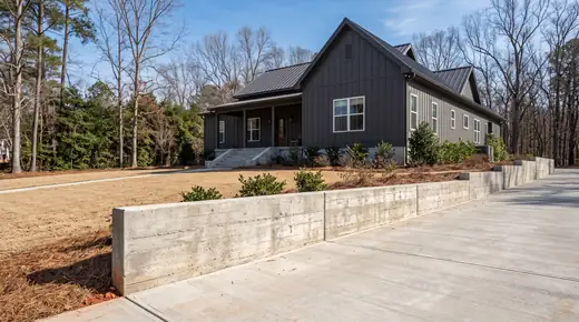 Board-formed concrete retaining wall holding a raised lawn at a charcoal farmhouse-modern home in Savannah, GA, in clear late-morning sun.