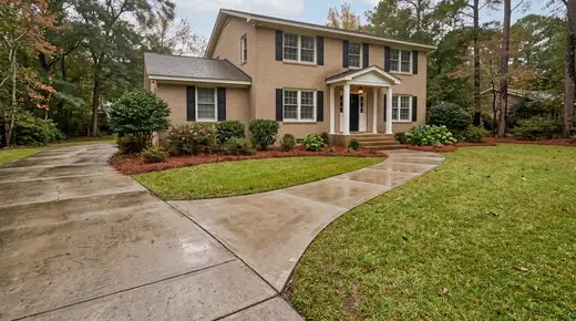 Concrete walkway meeting the driveway apron and front steps at a tan-brick colonial in Savannah, GA, after a rain shower.