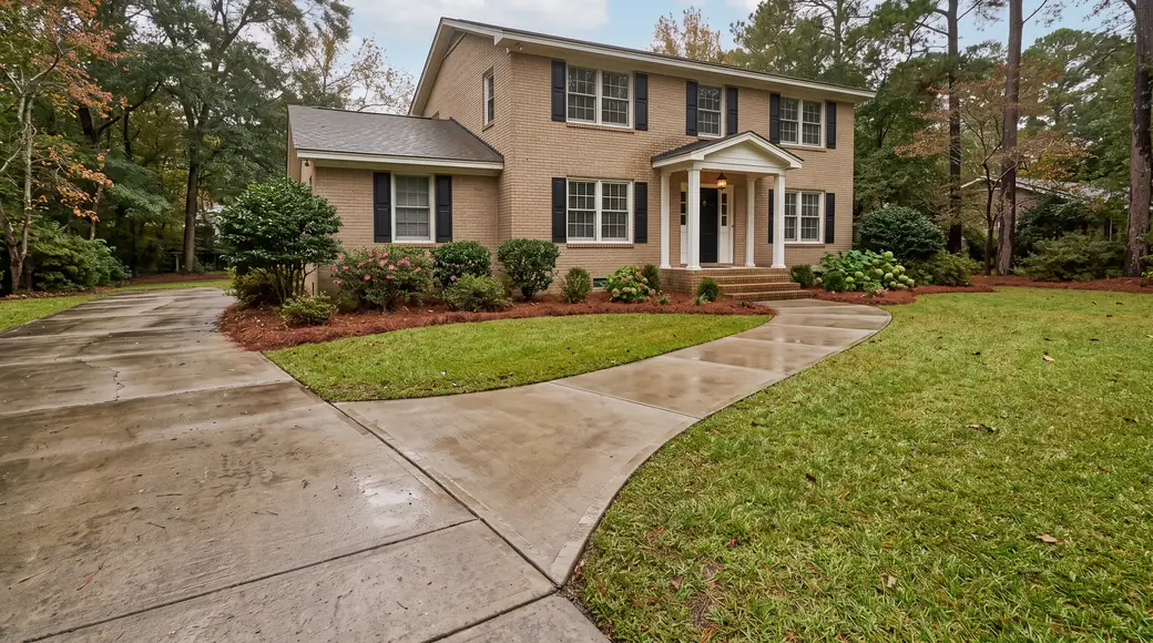 Concrete walkway meeting the driveway apron and front steps at a tan-brick colonial in Savannah, GA, after a rain shower.
