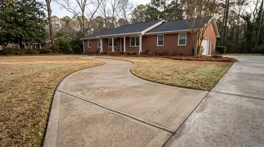 Curving concrete walkway crossing a front yard at a red-brick ranch home in Savannah, GA, in early morning light.