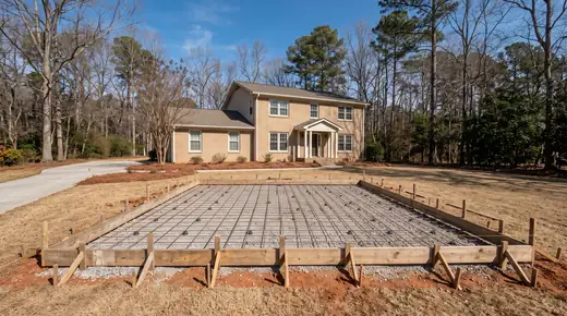Concrete patio formed and prepped, base and rebar visible before the pour at a tan-brick colonial in Savannah, GA, in clear late-morning sun.