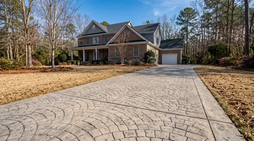 Stamped concrete driveway in a fan-set cobblestone pattern at a brick-and-siding two-story home in Savannah, GA, in clear late-morning sun.
